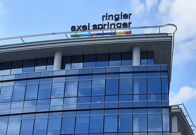Moderne Glasfassade eines Bürogebäudes mit Schriftzug ringier axel springer oben am Dach.