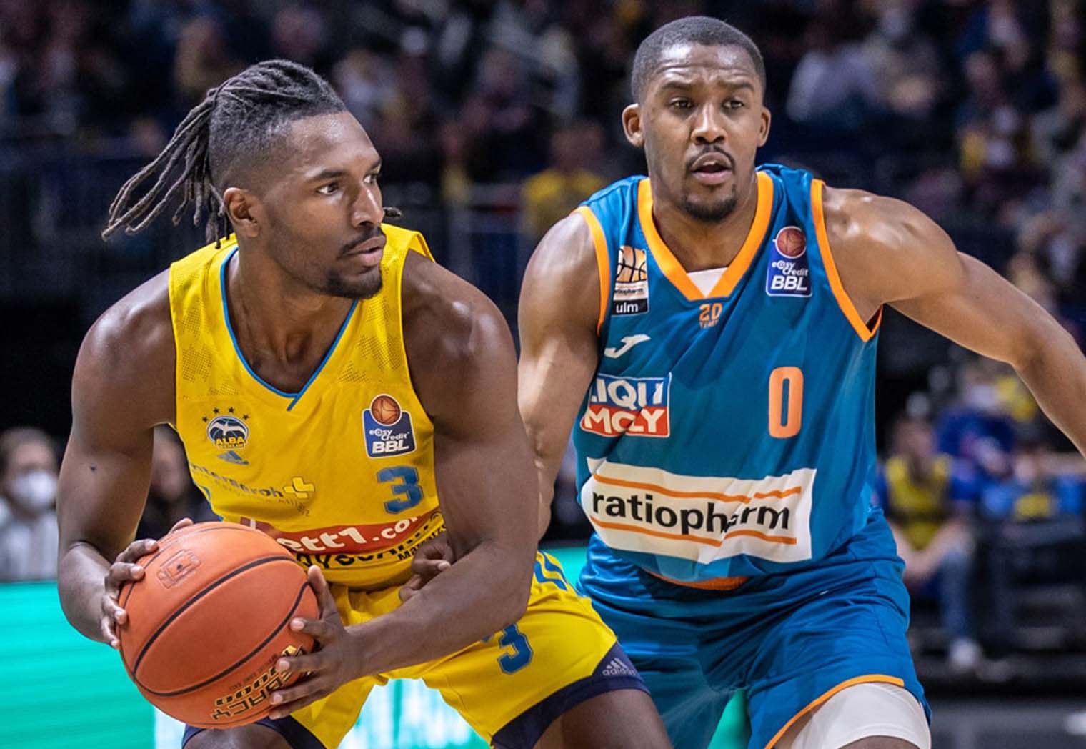 Zwei Basketballspieler in gelber und blauer Uniform kämpfen um den Ball auf dem Spielfeld.
