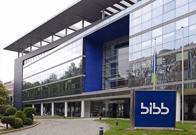 Modern glass building with BIBB sign and flags in front on a green lawn.
