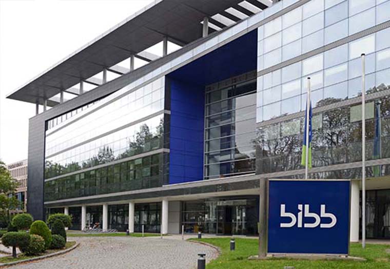 Modern glass building with BIBB sign and flags in front on a green lawn.