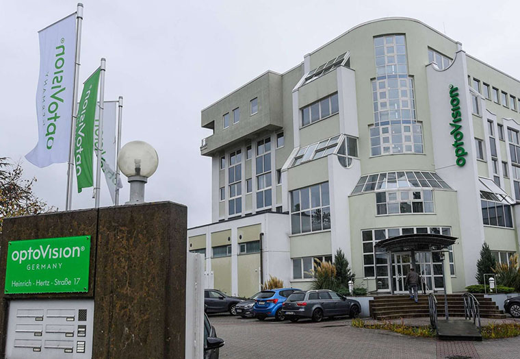 Modern office building of optoVision with company flags and green sign by the entrance in Germany.