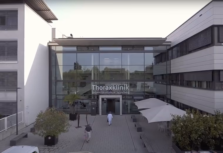 Eingang der Thoraxklinik am Universitätsklinikum Heidelberg mit Personen und Außensitzbereich.