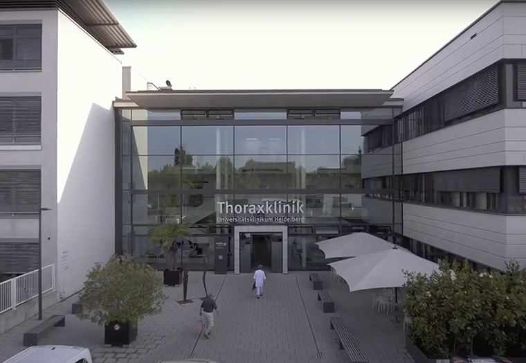 Eingang der Thoraxklinik am Universitätsklinikum Heidelberg mit Personen und Außensitzbereich.