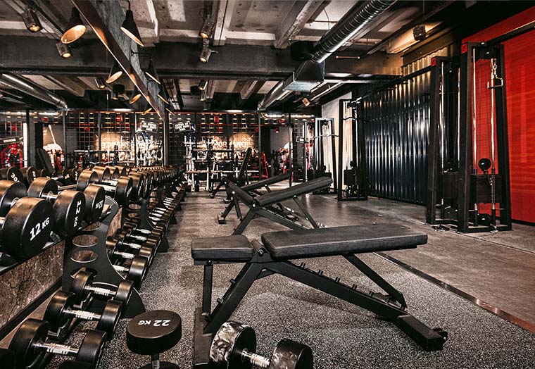 Innenansicht eines Fitnessstudios mit verstellbaren Hantelbänken und Hanteln an der Spiegelfront.