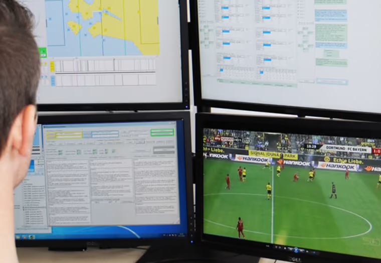 Person vor vier Monitoren, die Daten und ein Fußballspiel zwischen Dortmund und Bayern zeigen.