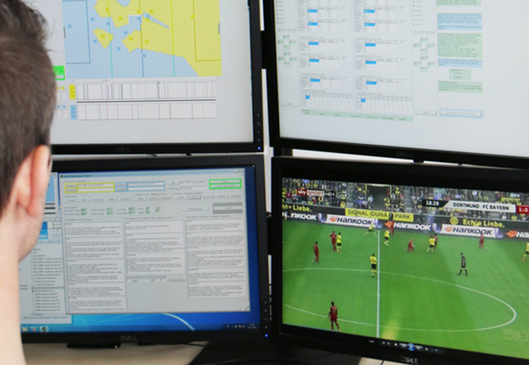 Person vor vier Monitoren, die Daten und ein Fußballspiel zwischen Dortmund und Bayern zeigen.