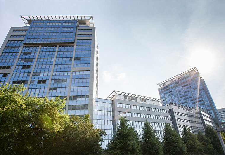 Moderne Bürotürme mit Glasfassade bei sonnigem Himmel und Bäumen im Vordergrund.