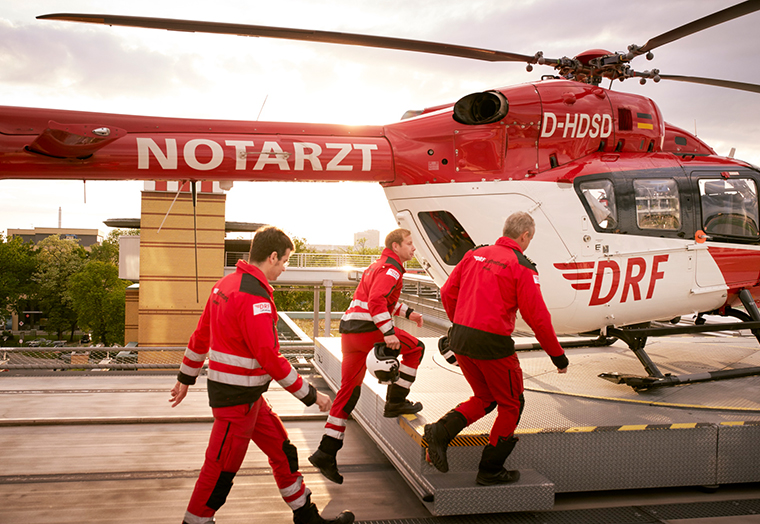 Drei Notarzt mit roten Uniformen steigen in einen Hubschrauber der DRF Luftrettung.
