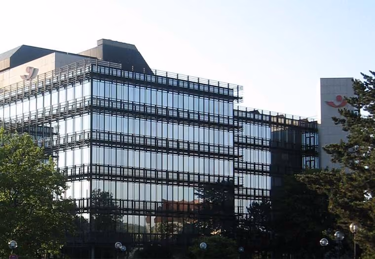 Modernes Bürogebäude mit Glasfassade, umgeben von Bäumen und klarem Himmel.