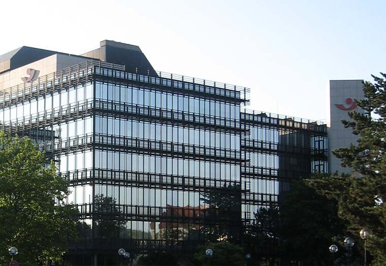 Modernes Bürogebäude mit Glasfassade, umgeben von Bäumen und klarem Himmel.