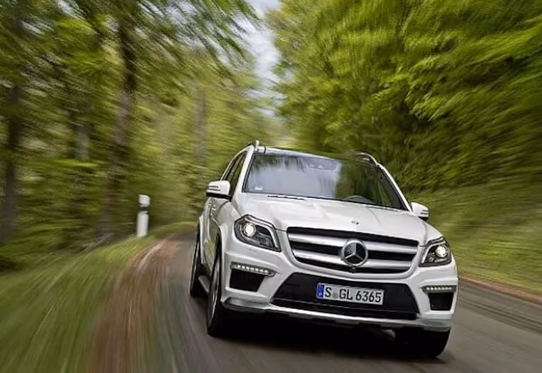 Weißer Mercedes-Benz SUV fährt zügig auf kurviger Straße umgeben von grünen Bäumen.
