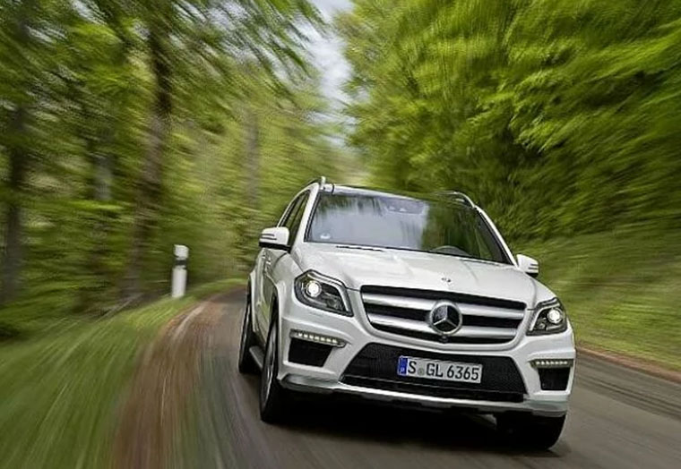 Weißer Mercedes-Benz SUV fährt zügig auf kurviger Straße umgeben von grünen Bäumen.