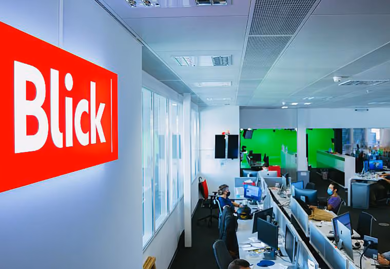 Blick-Logo an Wand in einem modernen Büro mit Mitarbeitern an Computern.