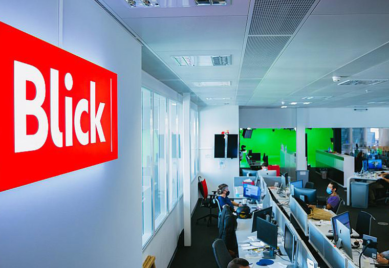 Blick-Logo an Wand in einem modernen Büro mit Mitarbeitern an Computern.