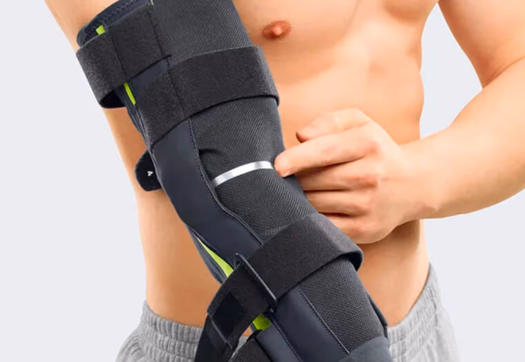Eine Person trägt eine schwarze Ellenbogenbandage mit Klettverschlüssen und zeigt darauf.