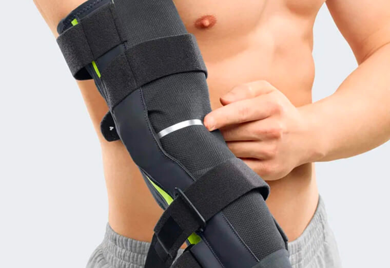 Eine Person trägt eine schwarze Ellenbogenbandage mit Klettverschlüssen und zeigt darauf.