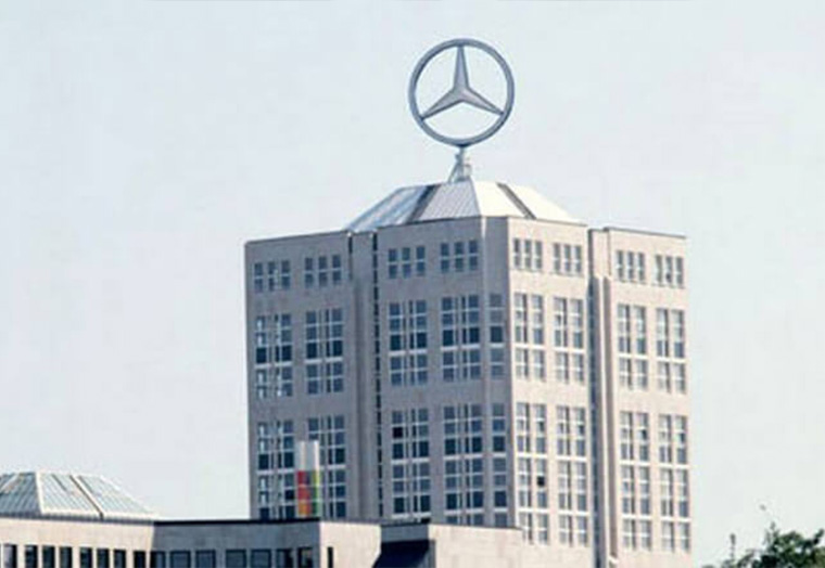 Hochhaus mit großem Mercedes-Stern auf dem Dach unter klarem Himmel.
