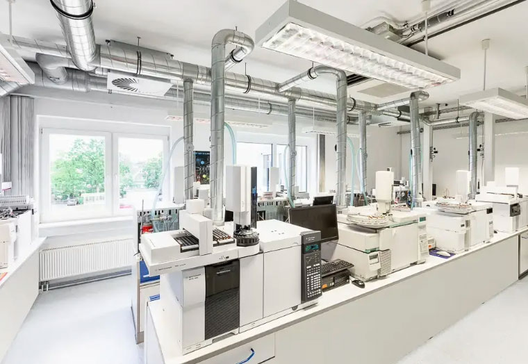 Modernes Labor mit mehreren analytischen Geräten und Lüftungsschläuchen an der Decke.