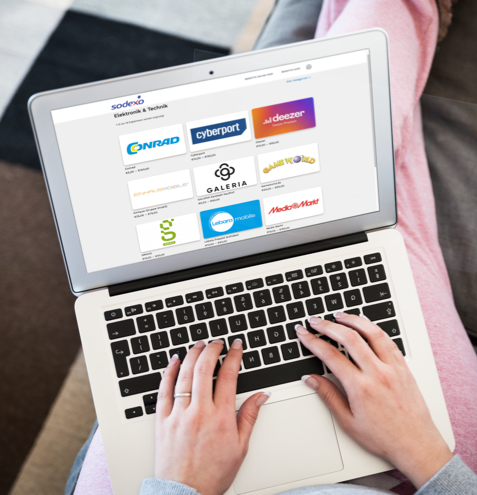 Person tippt auf einem Laptop mit Logos von Conrad, Cyberport, Deezer und weiteren Marken auf dem Bildschirm.