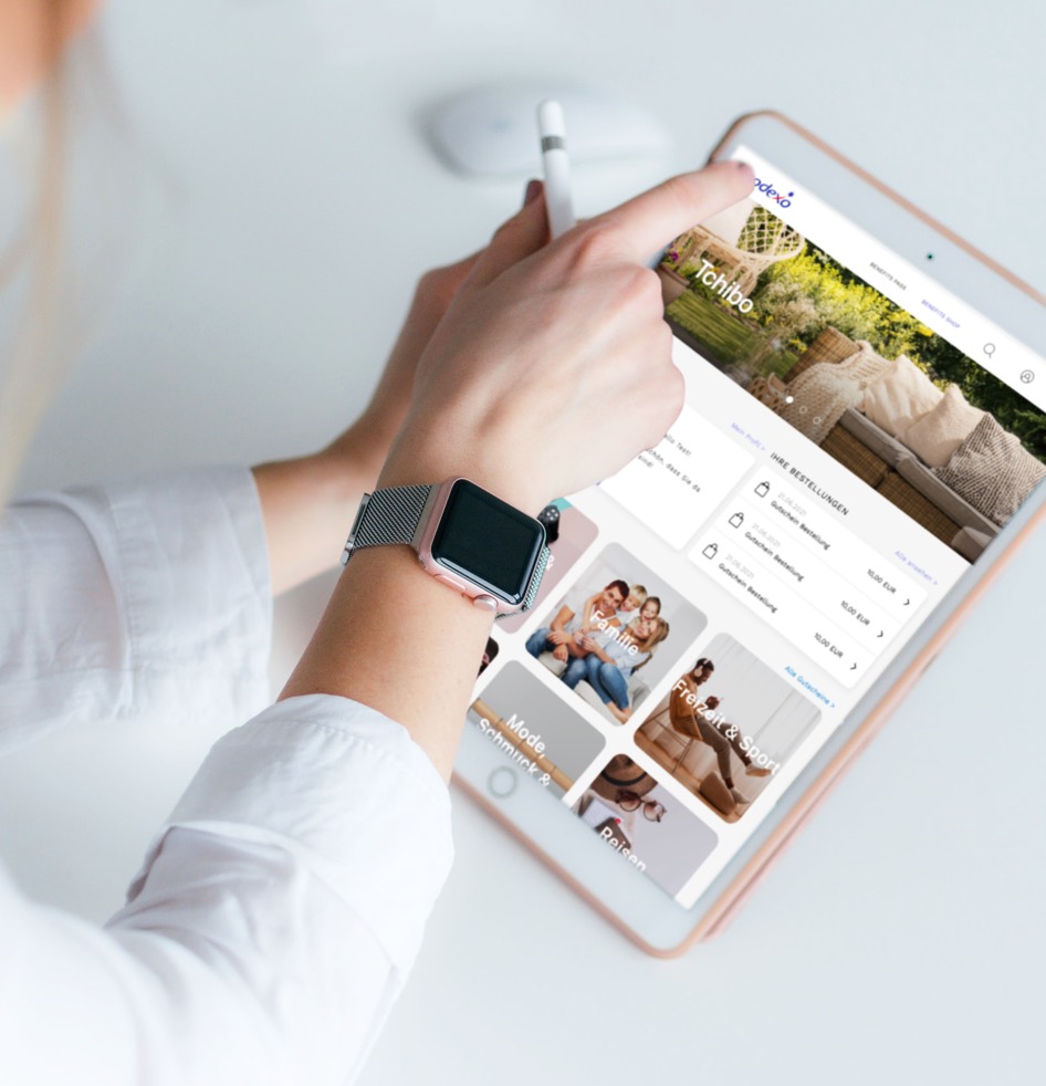 Person benutzt ein Tablet mit einem digitalen Einkaufsportal, trägt eine Smartwatch und hält einen Stift.