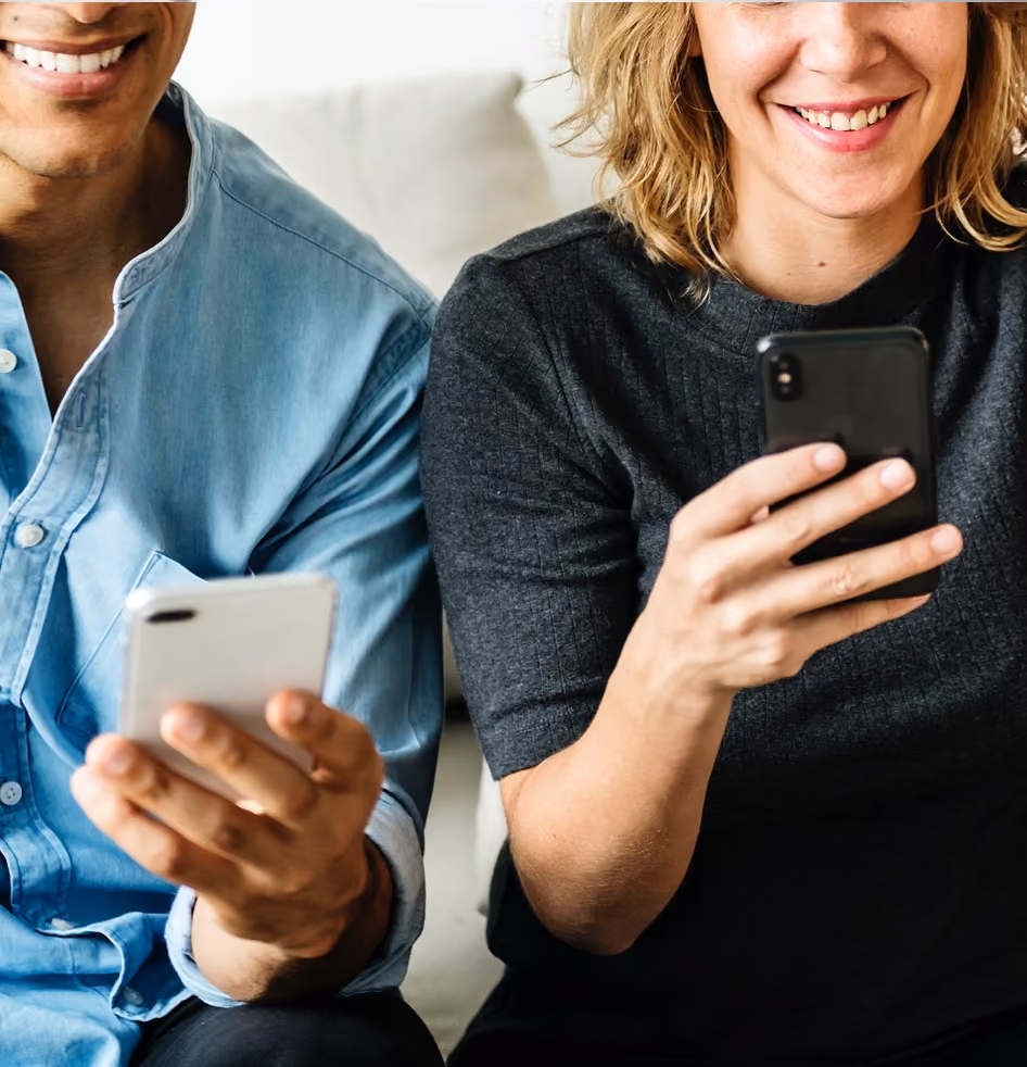 Zwei lächelnde Personen, die Smartphones halten und darauf schauen.