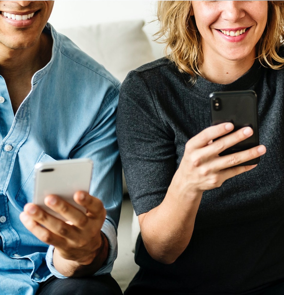 Zwei lächelnde Personen, die Smartphones halten und darauf schauen.