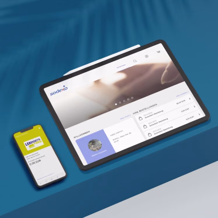 Tablet und Smartphone anzeigen die Sodexo-Plattform mit Gutscheinen und Benutzerprofil auf einem blauen Tisch.