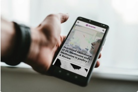 Hand hält Smartphone, darauf Webseite mit textlastigem Artikel und einem Foto zu sehen.