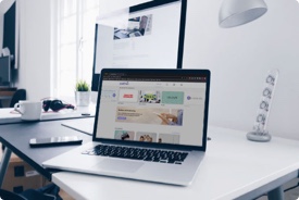 Laptop mit geöffneter Website steht auf einem weißen Tisch in einem modernen Büro.