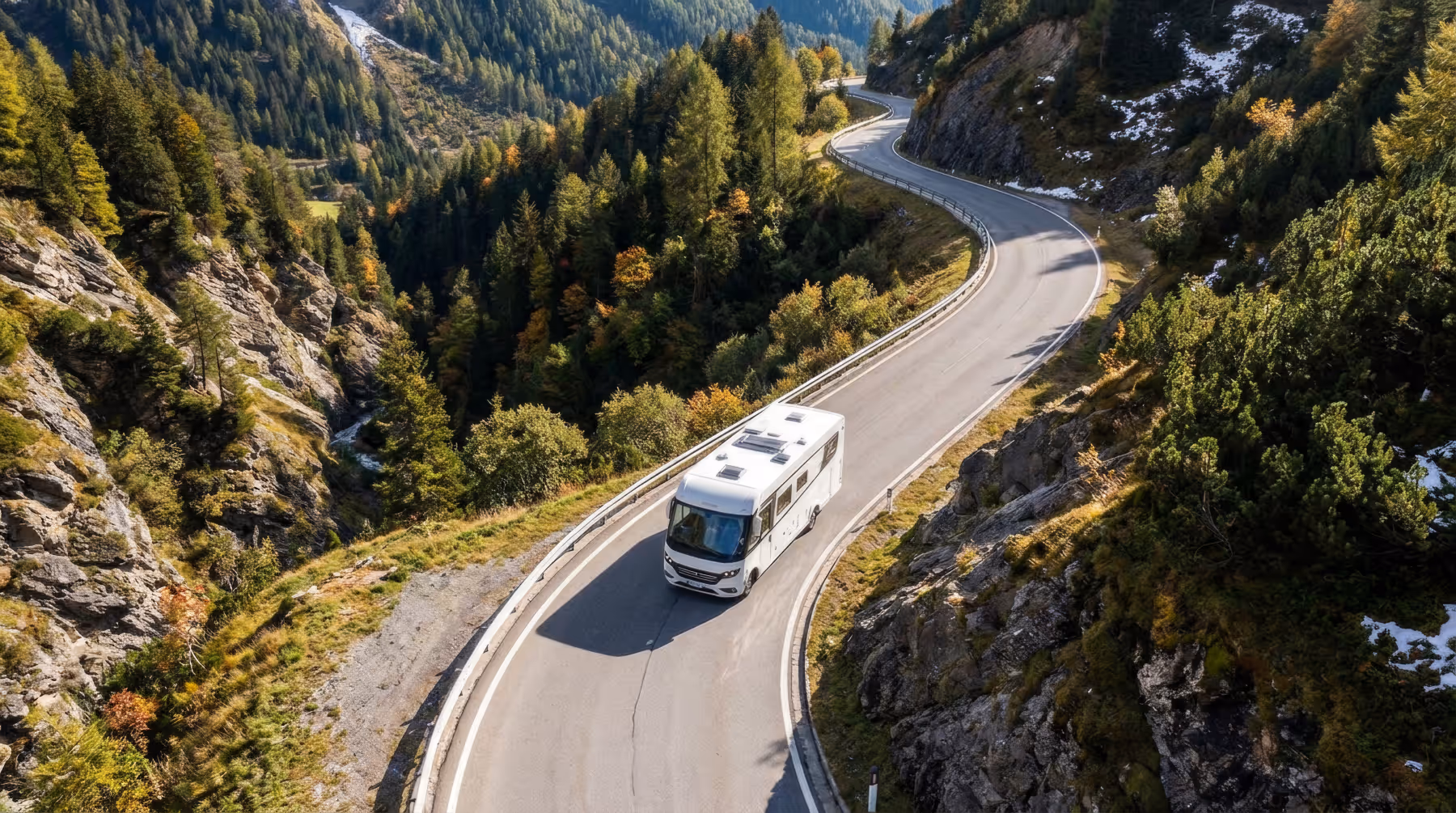 Wohnmobil fährt auf kurviger Bergstraße durch bewaldete Gebirgslandschaft mit Felsen und Vegetation.