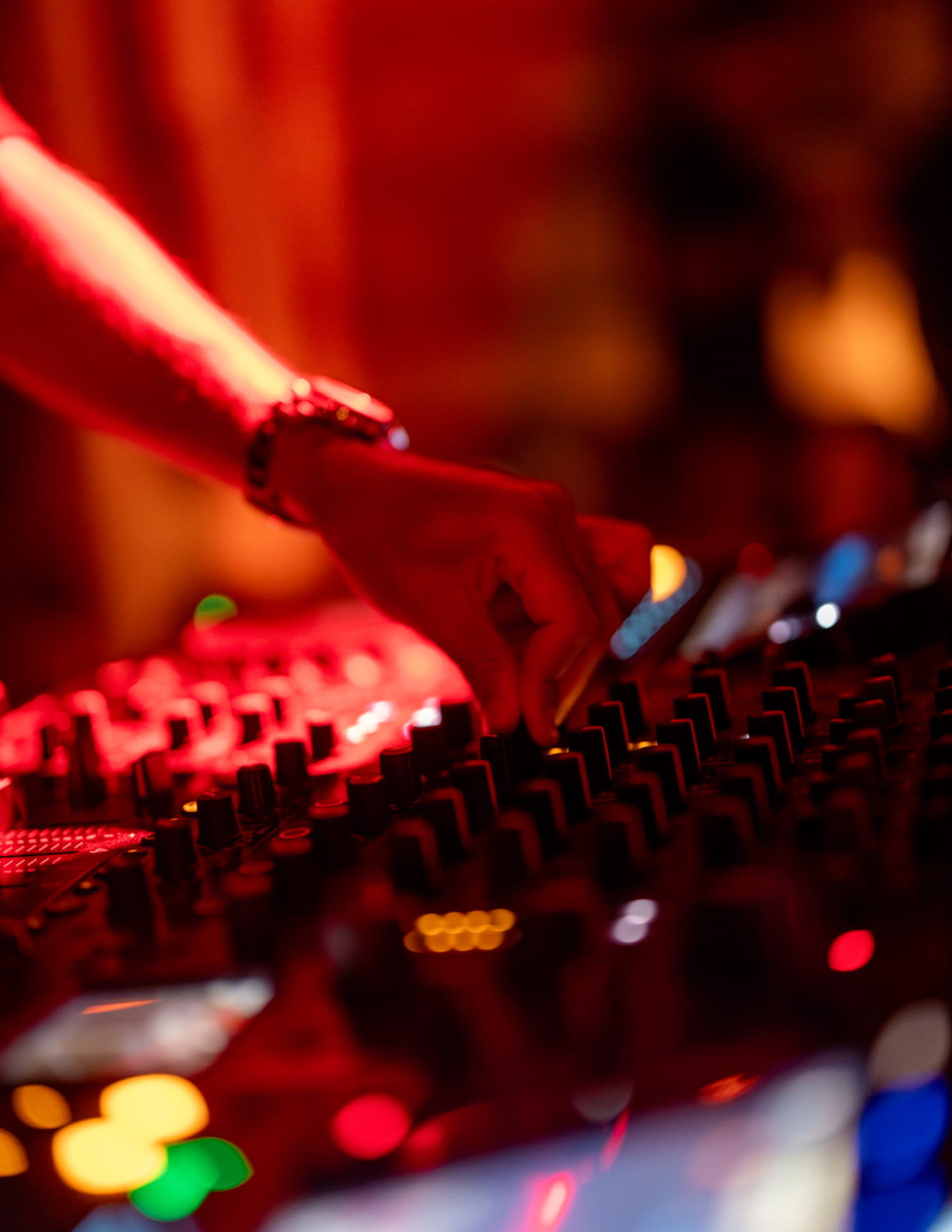 Main d'un DJ réglant les curseurs d'une table de mixage, ambiance nocturne aux lumières chaudes et bokeh coloré.