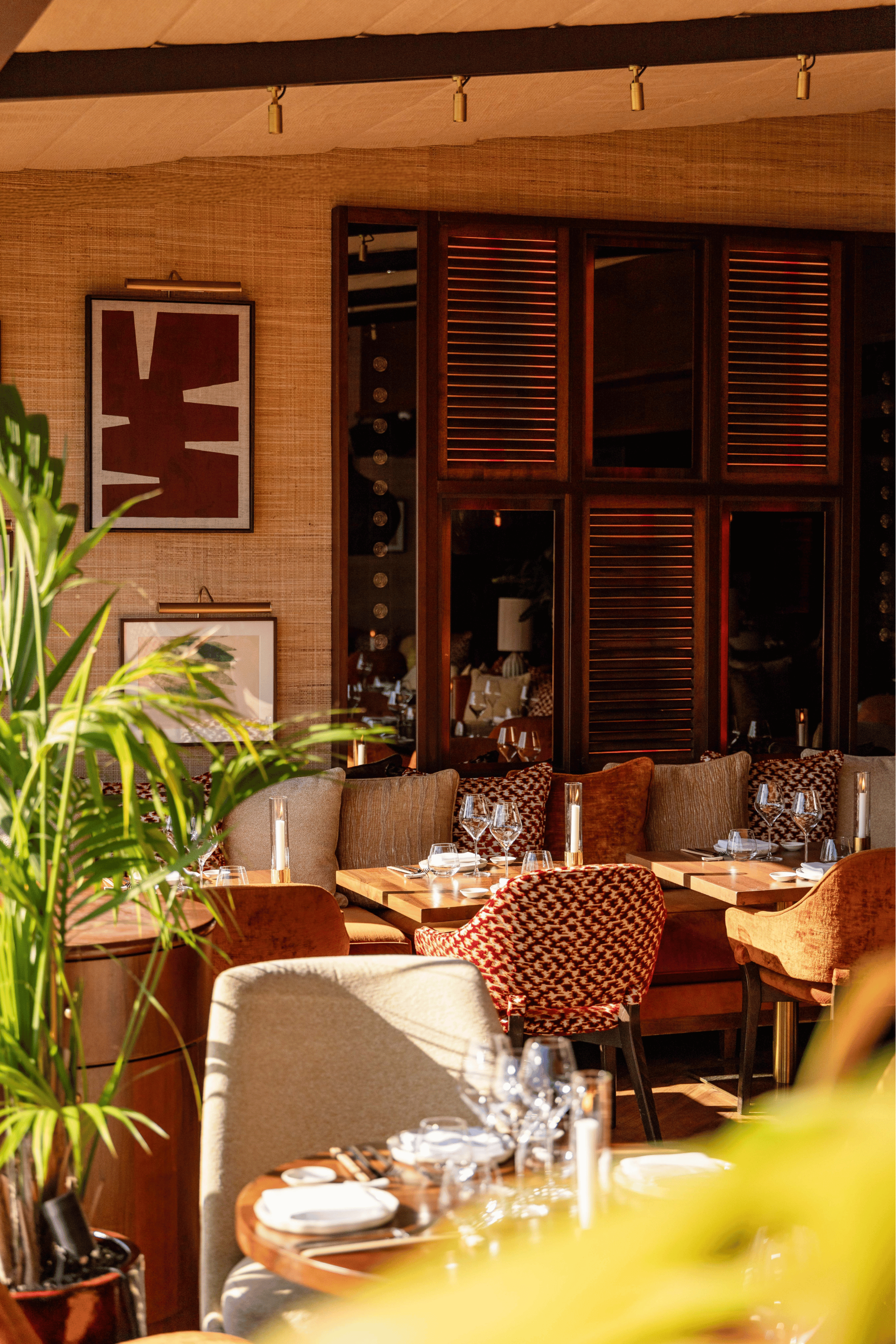 Salle de restaurant à l'ambiance chaleureuse, plante verte au premier plan, tables dressées et paravent en bois ajouré en arrière-plan.