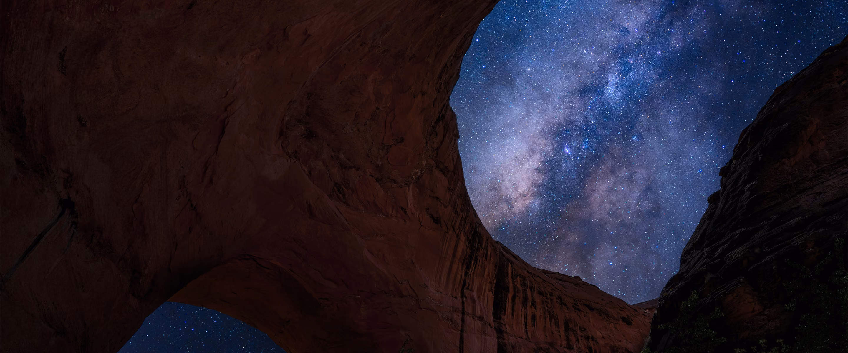 Starry night sky with Milky Way visible through a natural rock arch formation.