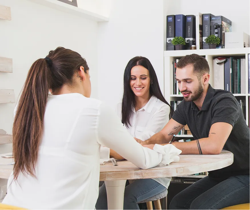 Three people sitting around a table in discussion, with bookshelves in the background.