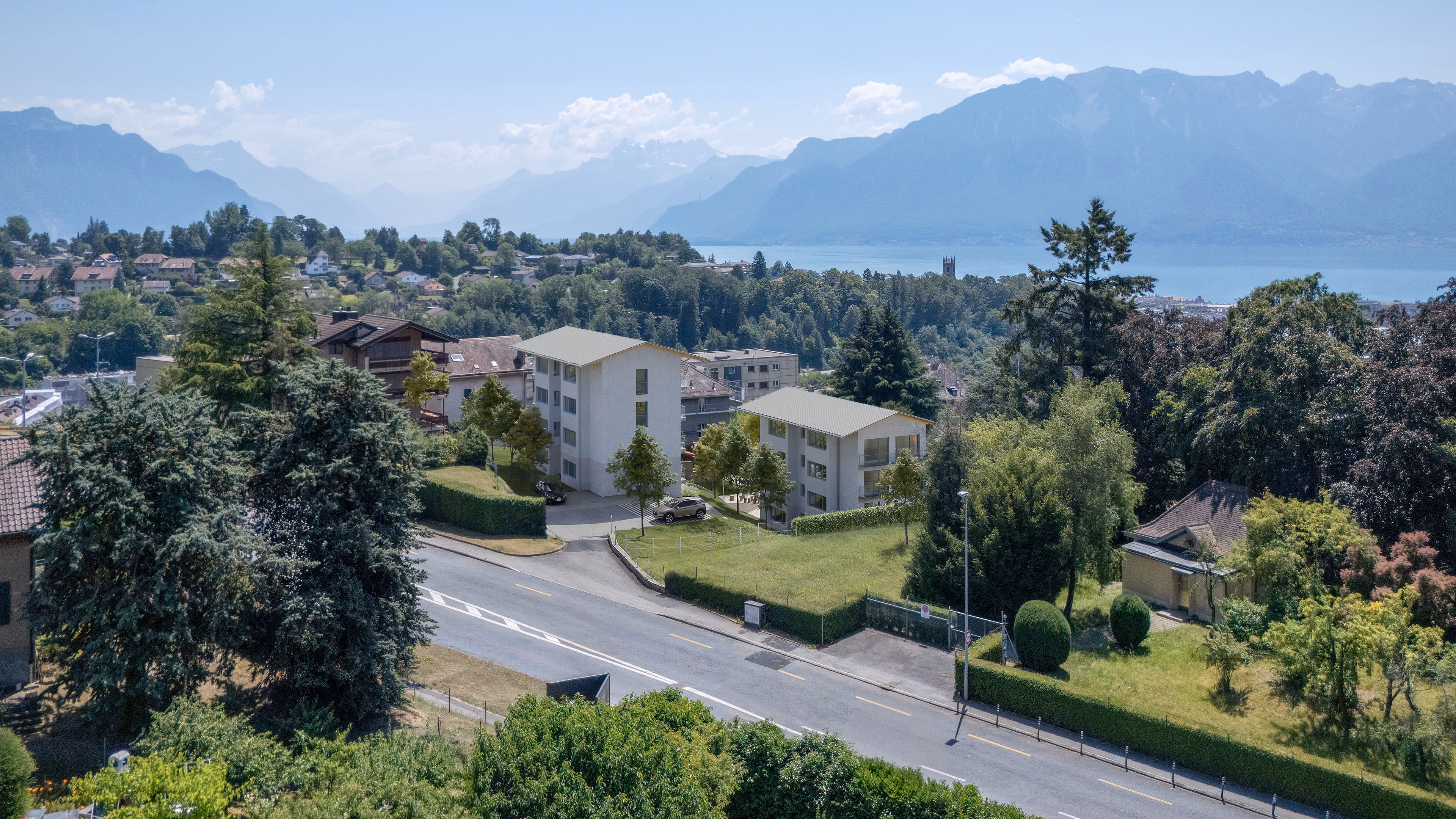 Vue aérienne de maisons résidentielles avec un lac et des montagnes en arrière-plan par temps clair.