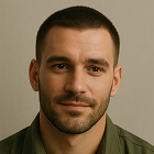 Close-up of a man with short dark hair, a trimmed beard, and a green shirt against a plain background.