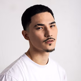 Headshot of a young man with short hair and facial hair wearing a white shirt against a plain background.