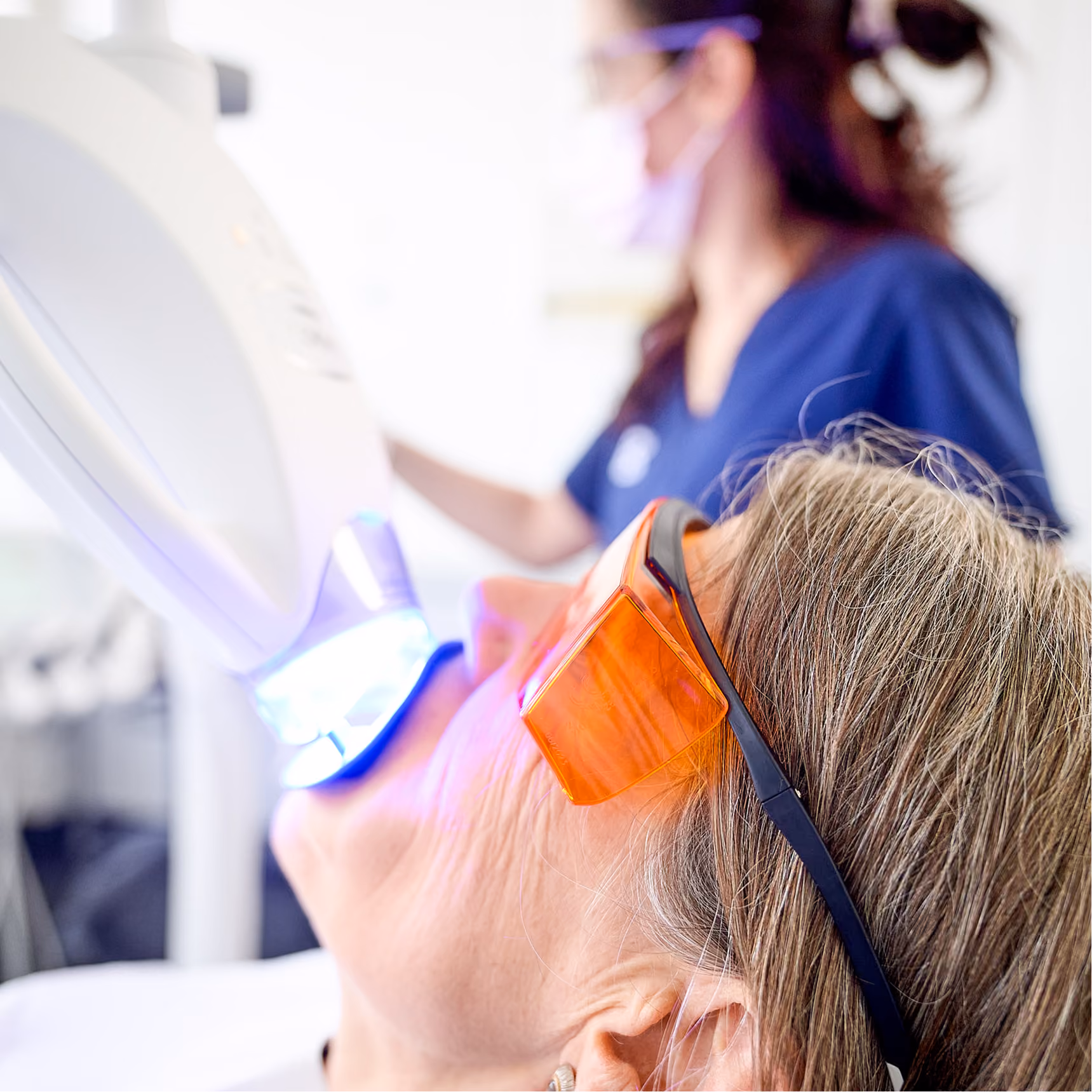 Patient trägt orange Schutzbrille bei zahnärztlicher Lichtbehandlung im Mundbereich.