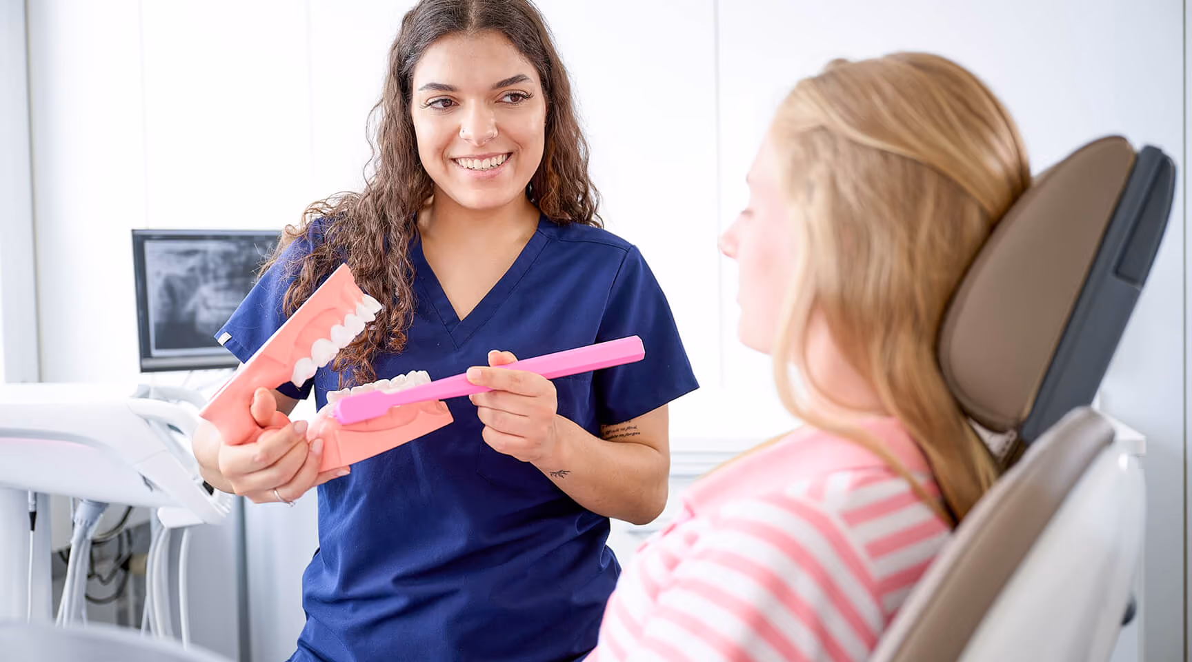 Zahnärztin zeigt einem Patienten mit einem Modell und einer riesigen Zahnbürste, wie man Zähne putzt.