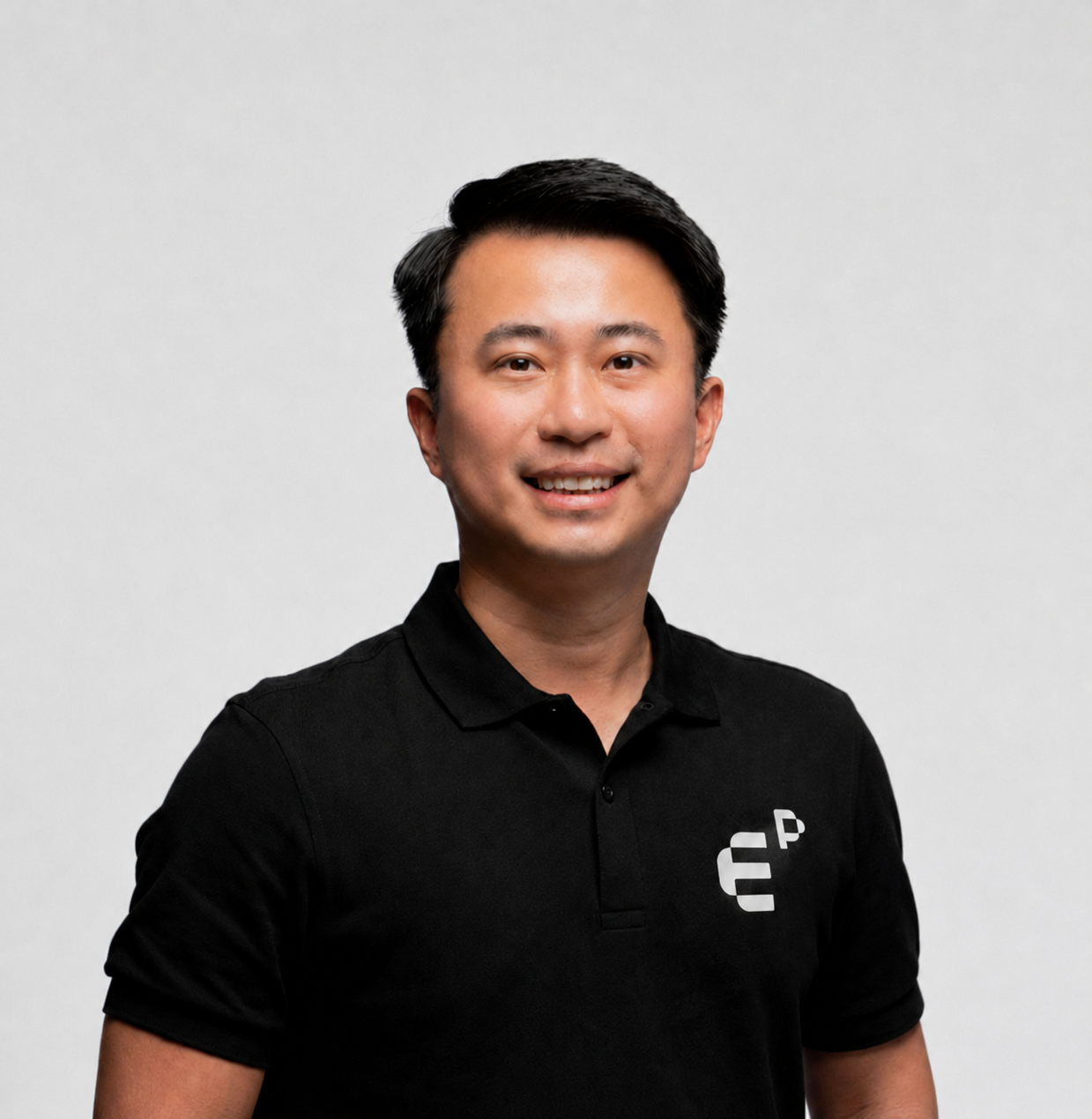 Smiling man with short black hair wearing a black polo shirt with a white logo on the chest.