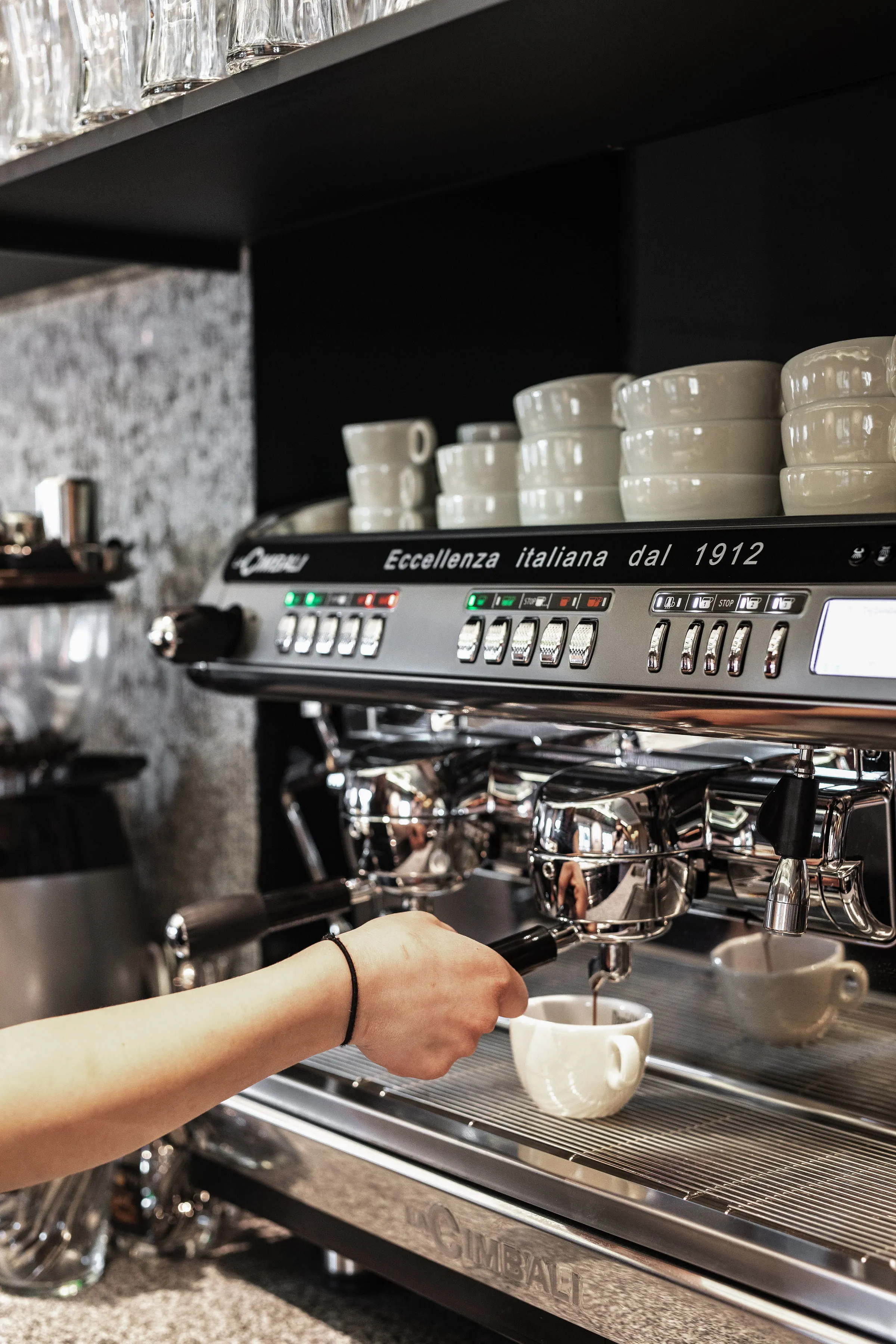 Hand bedient eine Espressomaschine, die Kaffee in eine weiße Tasse brüht.