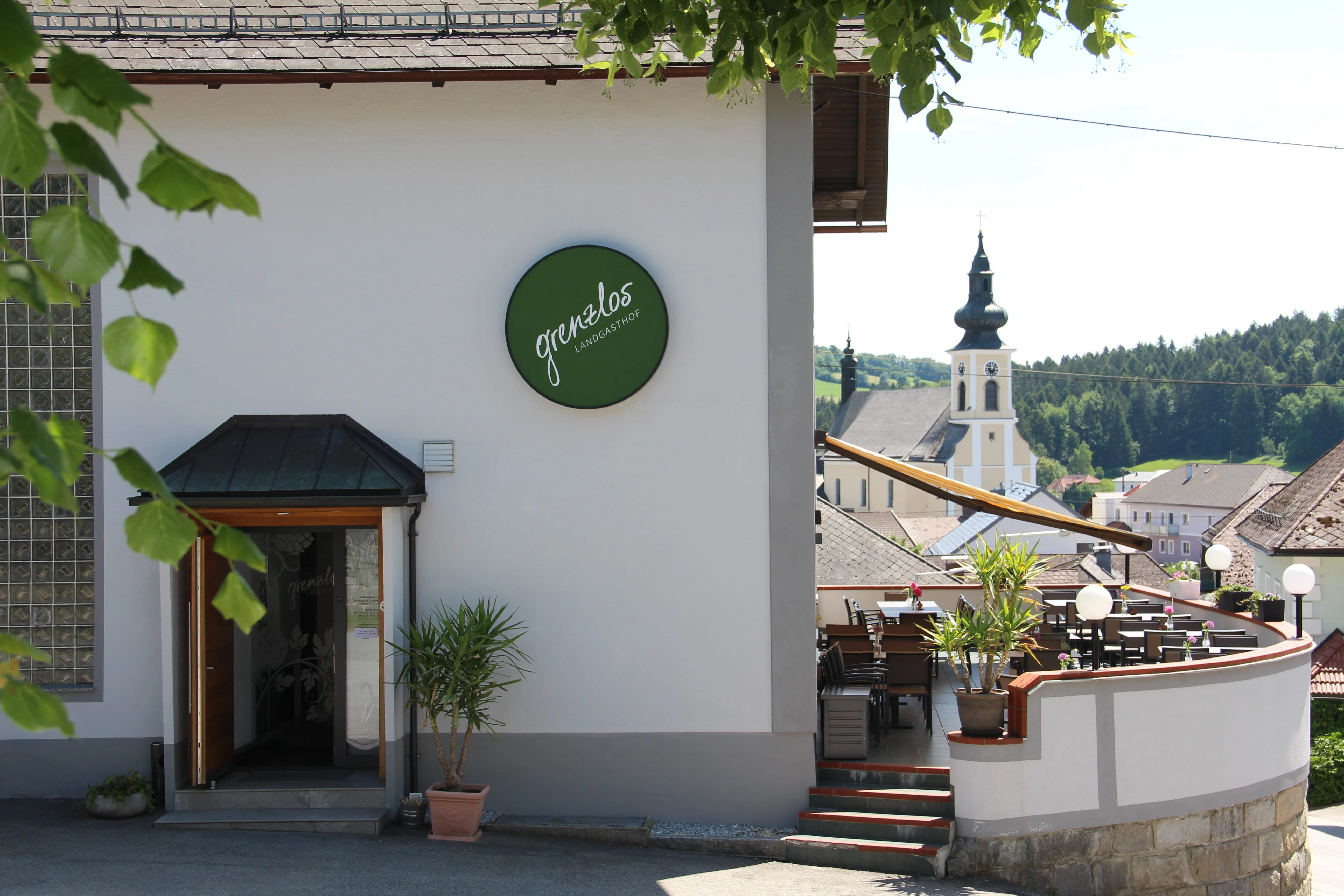 Außenterrasse des Landgasthofs Grenzlos mit Blick auf Kirchturm und bewaldete Hügel.