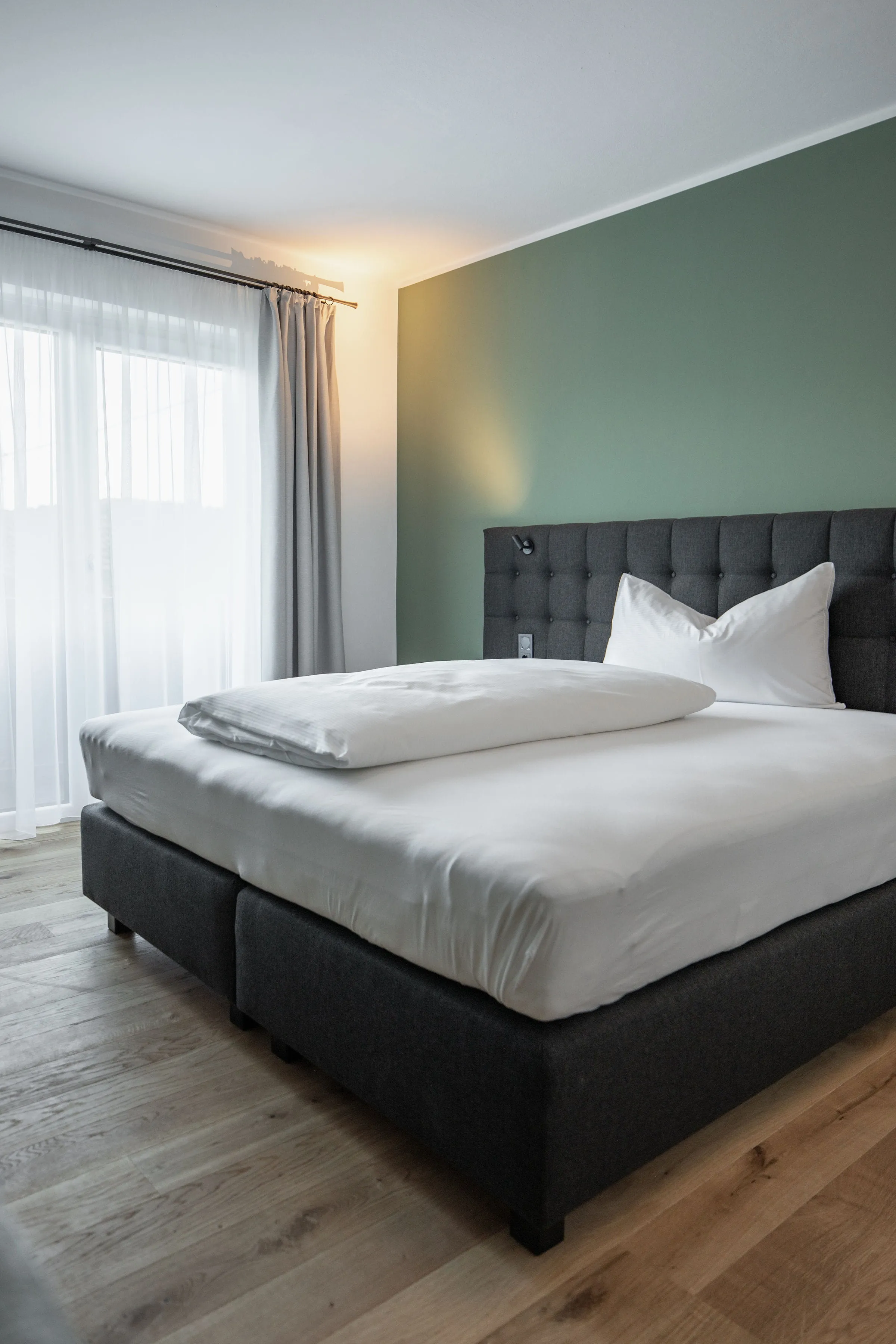 Modernes Schlafzimmer mit großem Bett, weißer Bettwäsche, grünem Akzentwand und Holzboden.