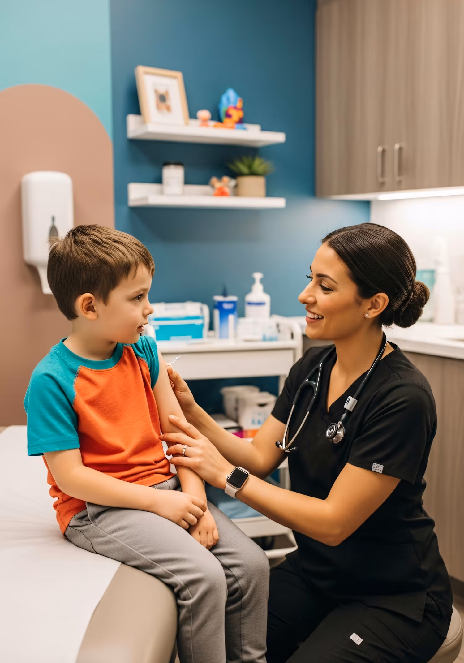 Nurse smiling and giving a vaccination to a young boy sitting on a medical exam table.