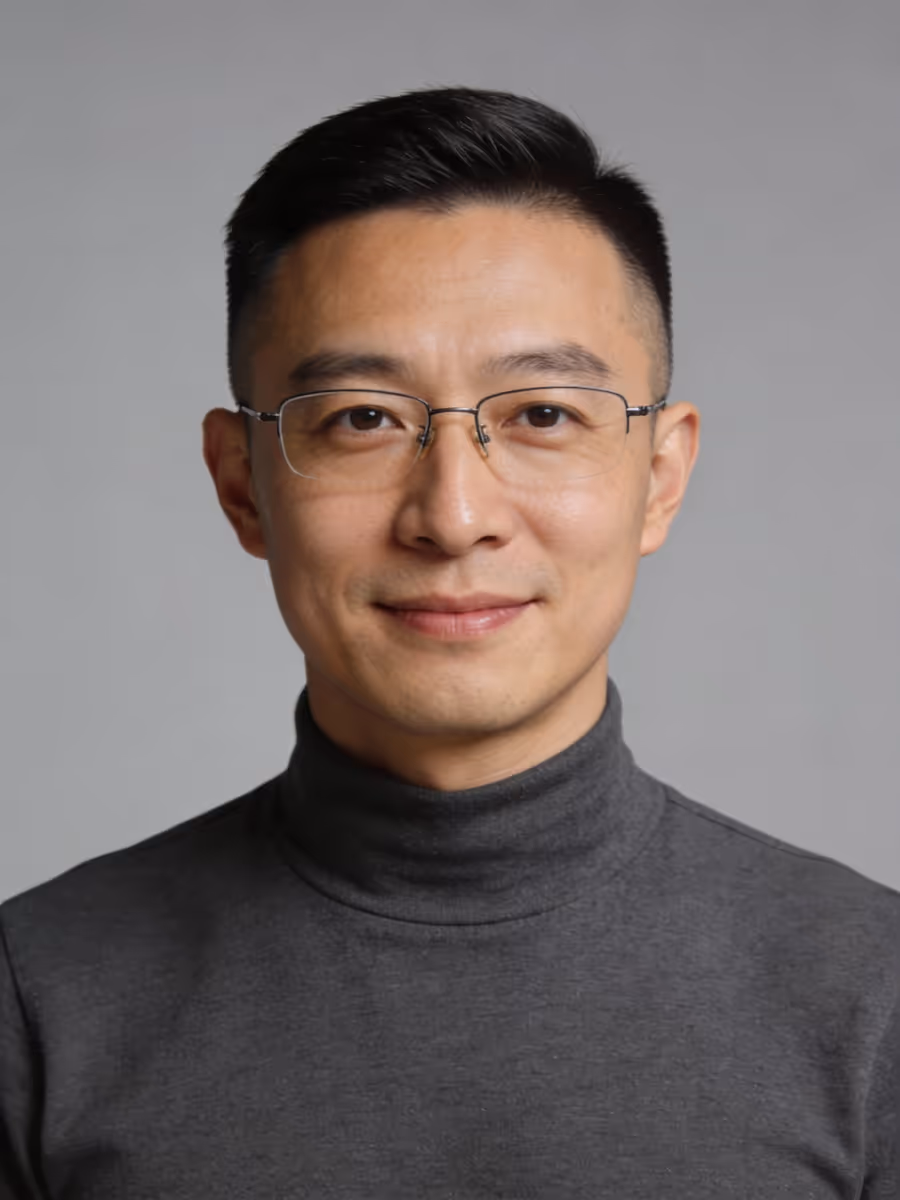 Portrait of a man wearing glasses and a dark gray turtleneck smiling against a gray background.