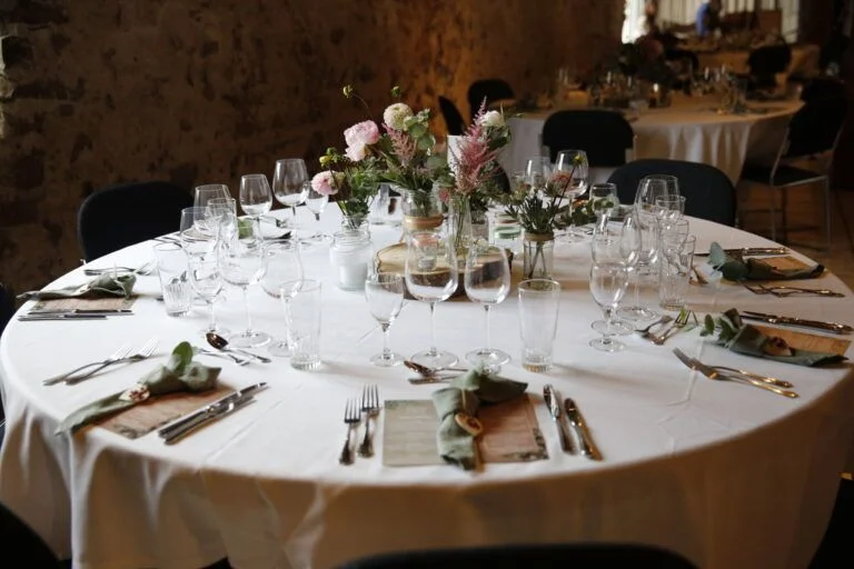 Elegantly plated dish with figs, greens, and sauce on white tablecloth with a glass of white wine.