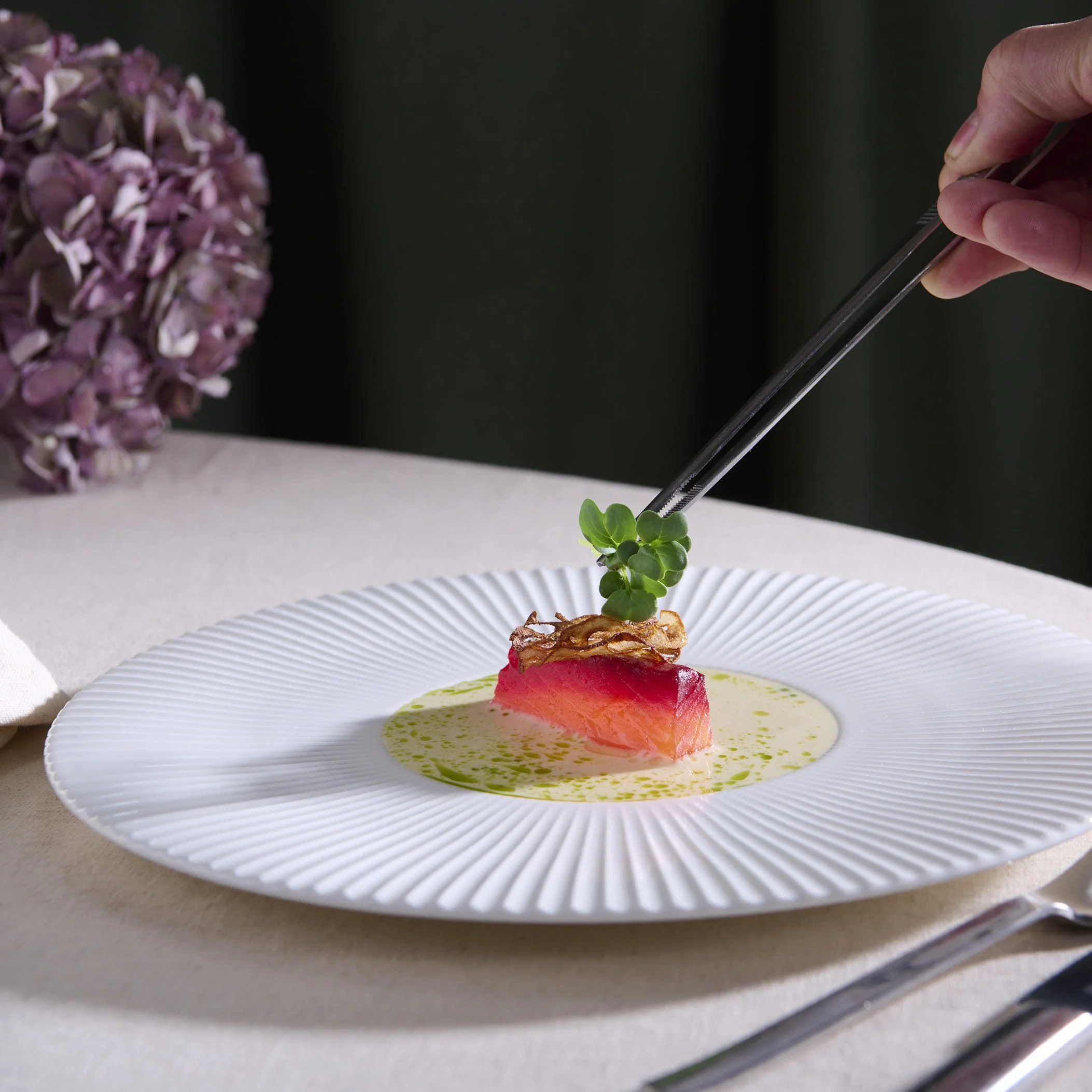 Close-up of a spoon lifting foam-covered gourmet dish with broth and garnishes in a bowl.