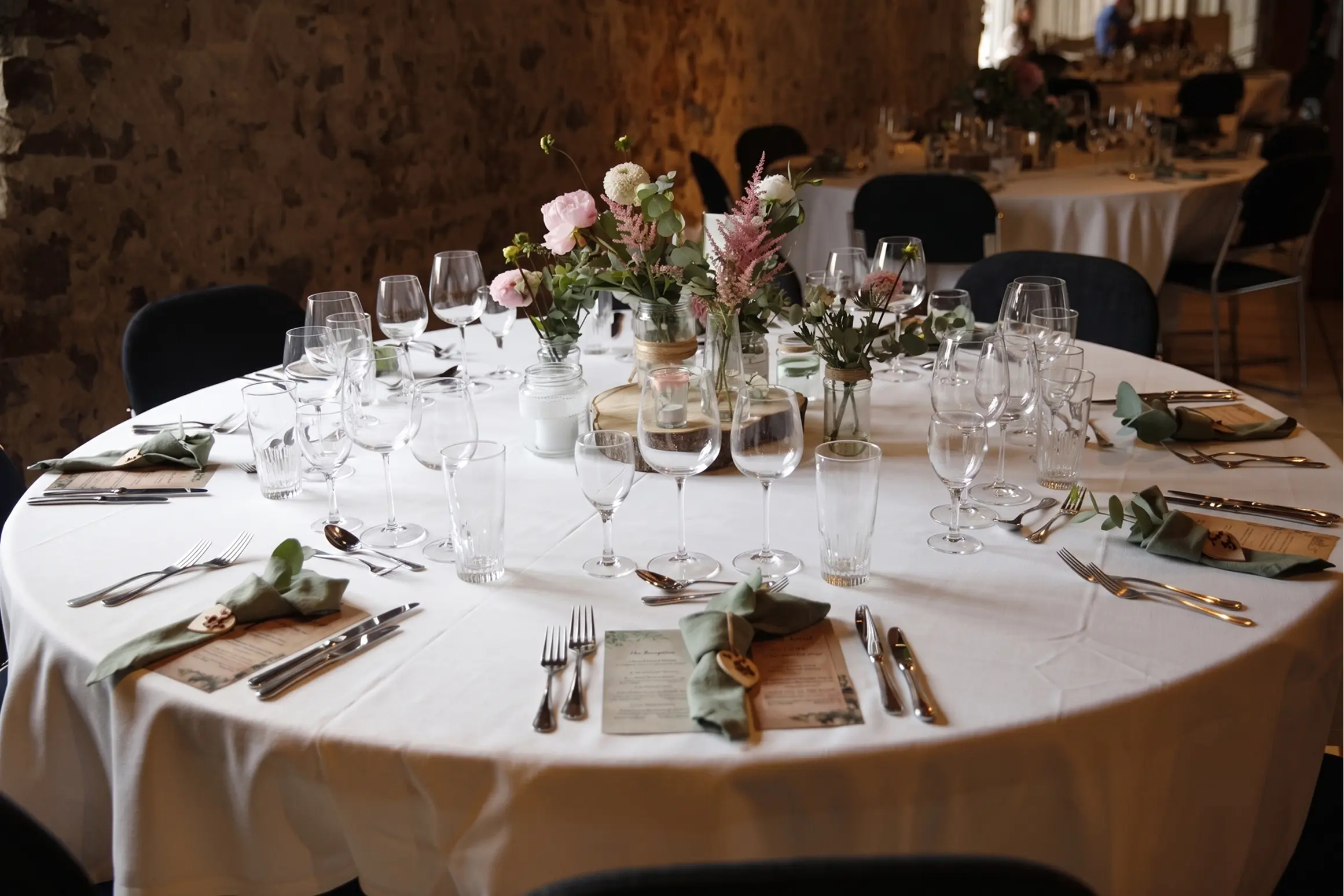 Hand pouring broth from small pitcher over a creamy pasta dish in a beige bowl on a white tablecloth.
