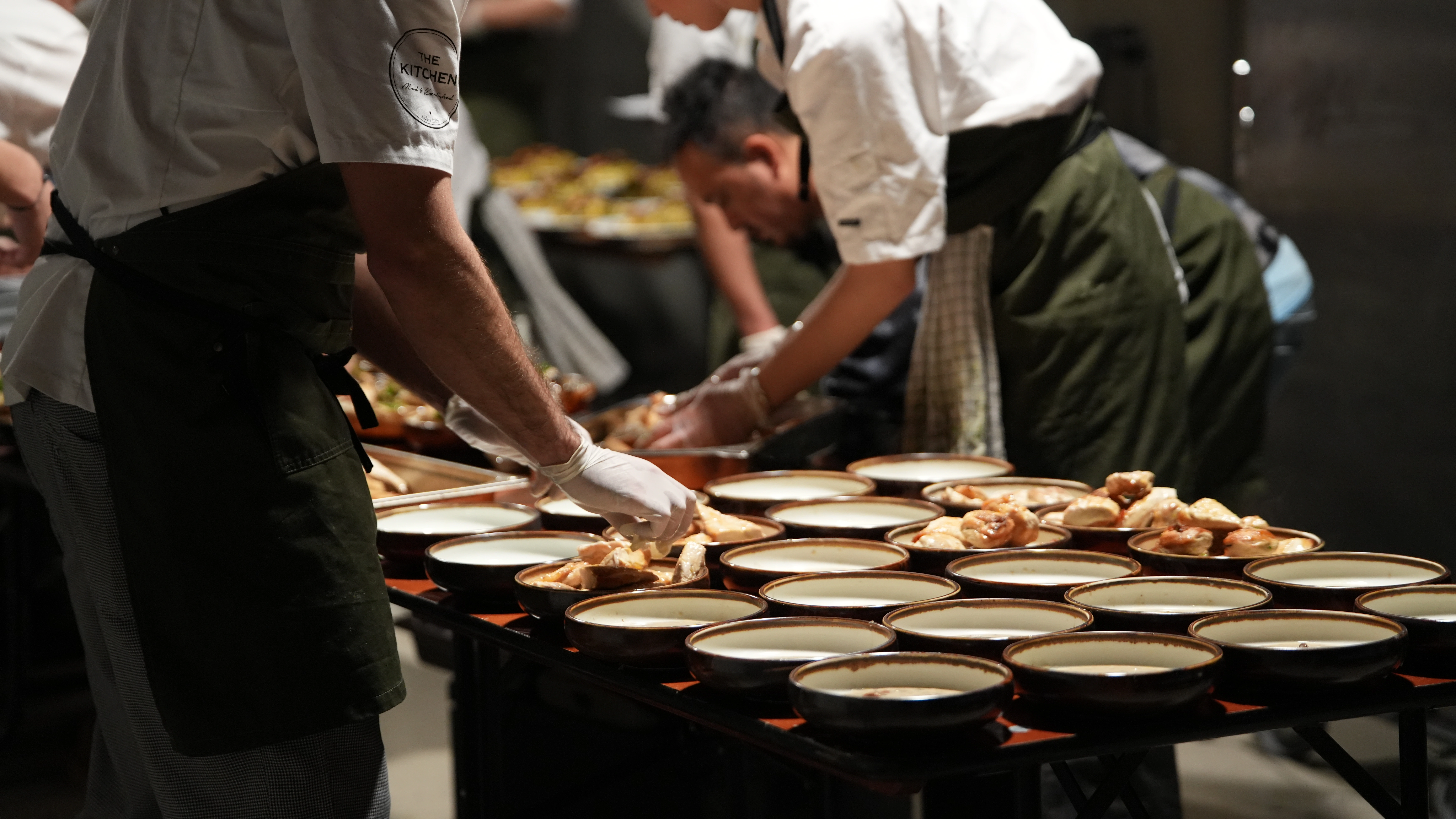 Closeup of gourmet appetizers with microgreens on small white plates in dim lighting.