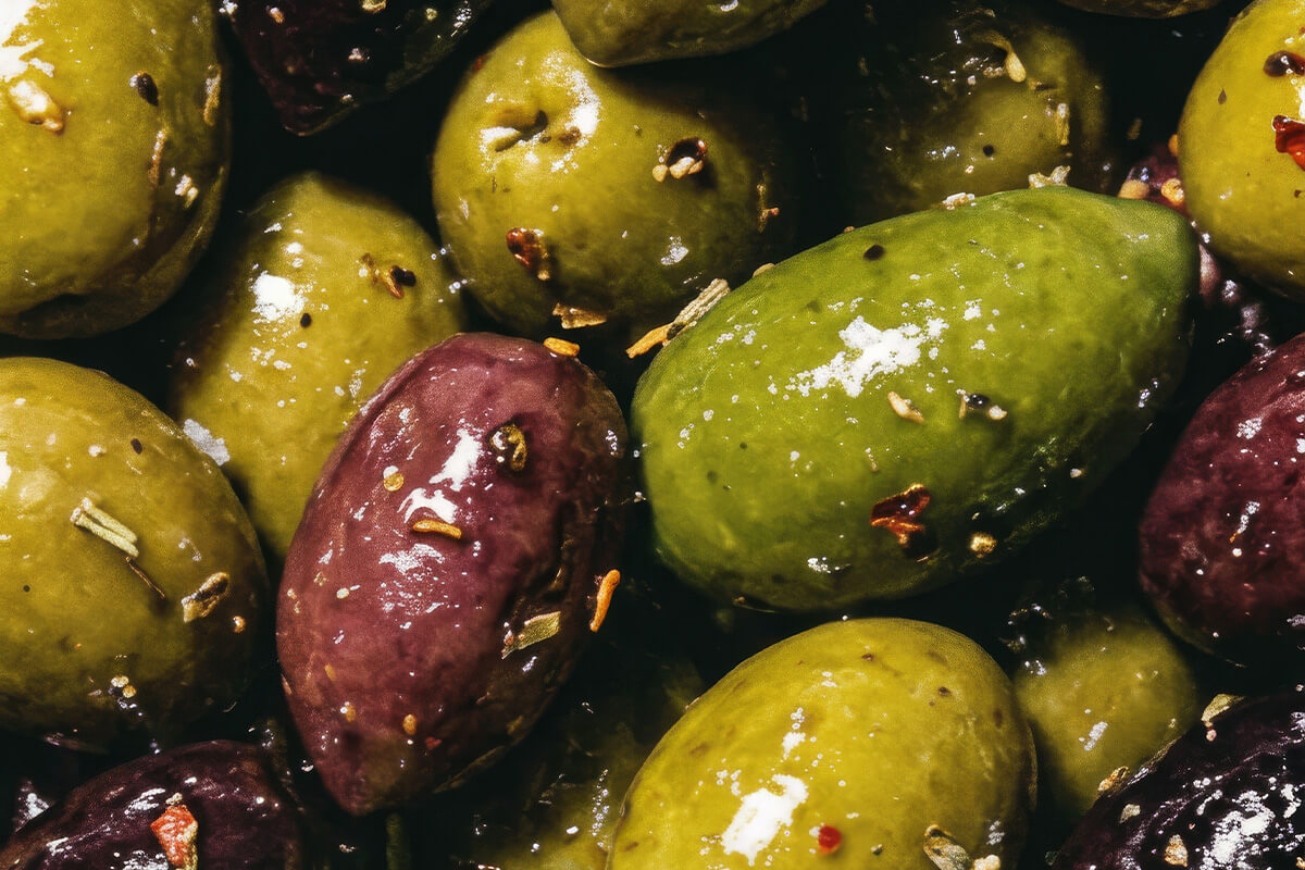 Nahaufnahme von grünen und violetten Oliven mit Gewürzen und grobem Salz.